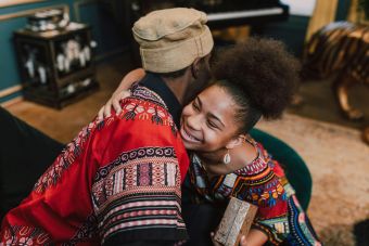 Smiling individuals in vibrant traditional clothing share a warm embrace during a Kwanzaa celebration.